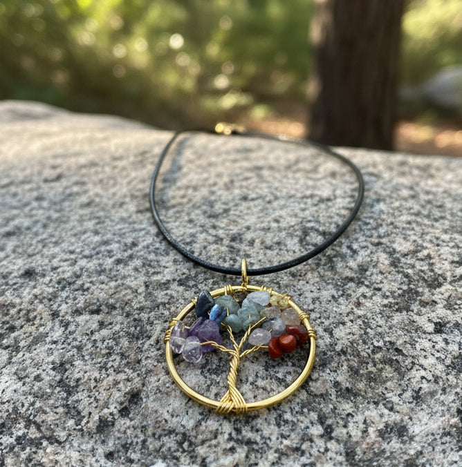 Tree of Life pendant with multicolored stones on a black cord against a wooden background