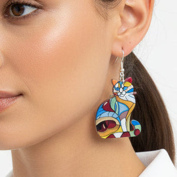 Woman wearing colorful cat earrings with a white sleeveless top on a light background